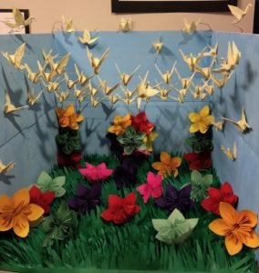 Origami diorama of flowers, grass and cranes.