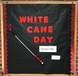 Bulletin board with words: White cane day and a small kiddie cane attached.