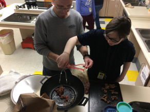 Student removing cooked meat from a skillet.