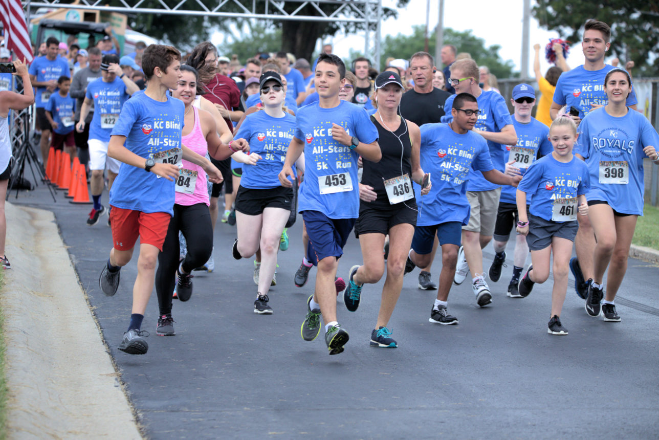 A large crowd of runners taking off from the starting line wearing smiling faces and the KSSB 5K t-shirts.