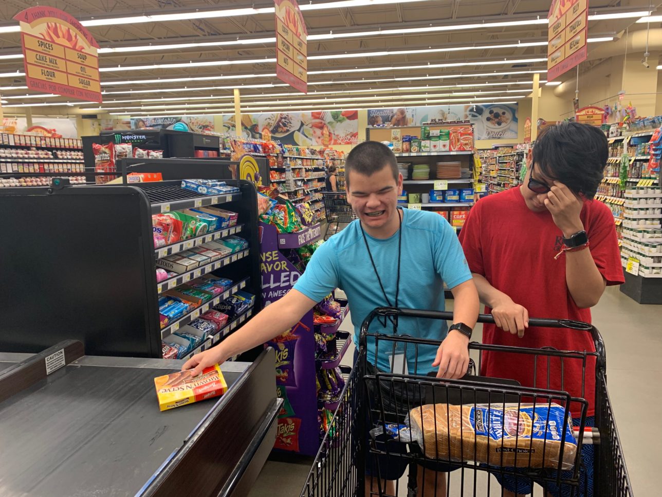 Two students with grocery items in cart.