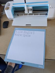 An electronic cutting machine that looks like a printer. It uses a blade and roller to cut out designs.