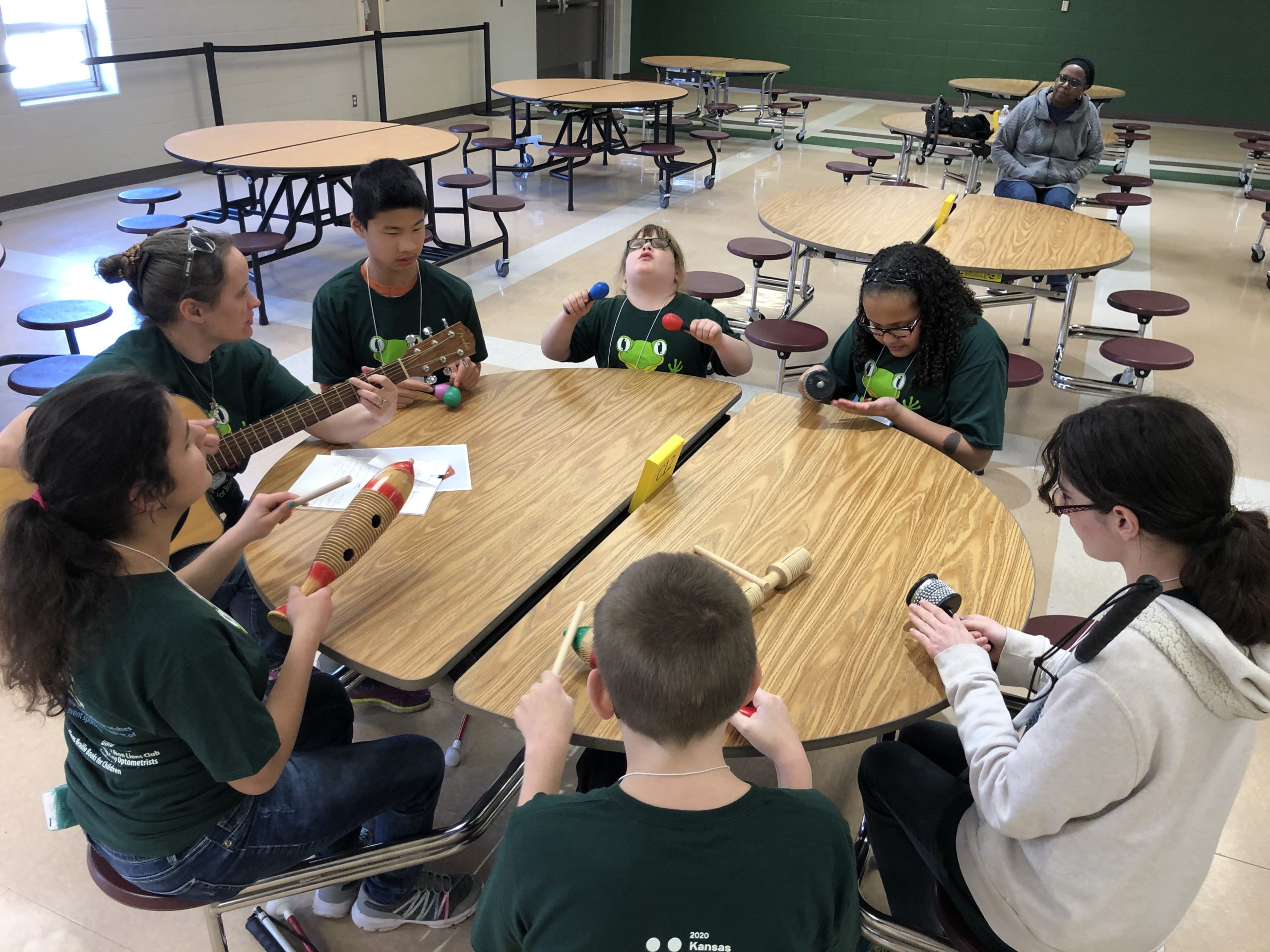 Several students wearing braille challenge shirts sitting around a circular table and holding musical instruments.