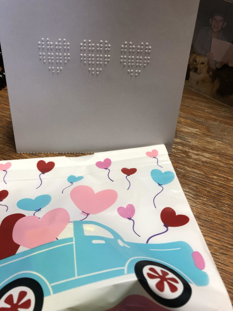 A card with three braille hearts and a plastic bag with hearts and a truck image on the front.
