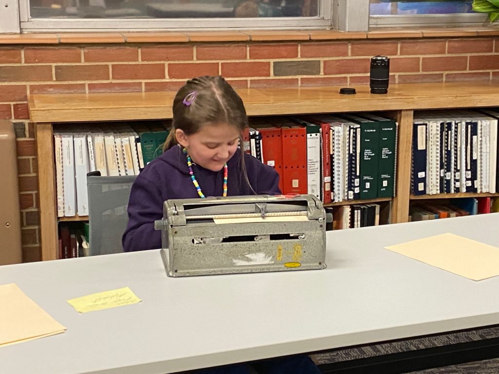A young child smiling while sitting in front of a braille writer.