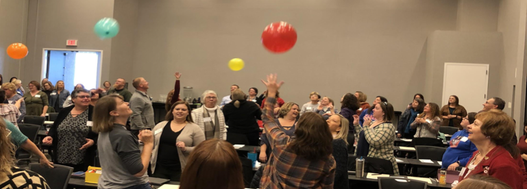 Teachers in a conference room, keeping balloons in the air.