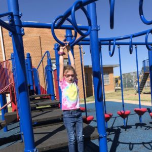 Girl Hanging From Monkey Bars At School Playground