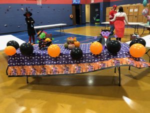 table decorated with orange and black balloons, The Count, and a witch ready for trunk-or-treat
