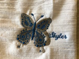embroidered blue and gold butterfly with Skyler written in blue to the right of the butterfly