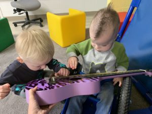 two boys playing on a purple guitar