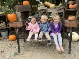two girls and a boy sitting on a bench with pumpkins behind them