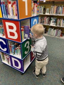 boy stands at a book case with letters and numbers on it look at books