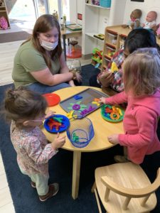 1 teacher and 2 girls sit at a table and play with letters on a cookie sheet
