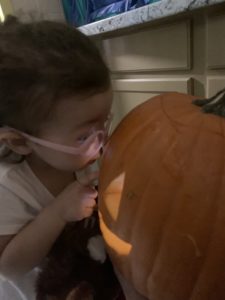 girl wearing glasses looks at a pumpkin that has been carved and light is shining out of the pumpkin