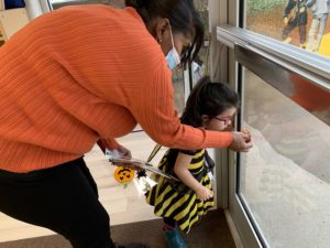 girl dressed as a bee looking at a teacher putting a pumpkin on the window