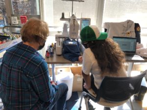 teacher and student sitting at an embroidery machine watching the machine create an image on fabric