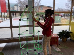 student standing and building a figure that has long green sticks held together by small grey joints