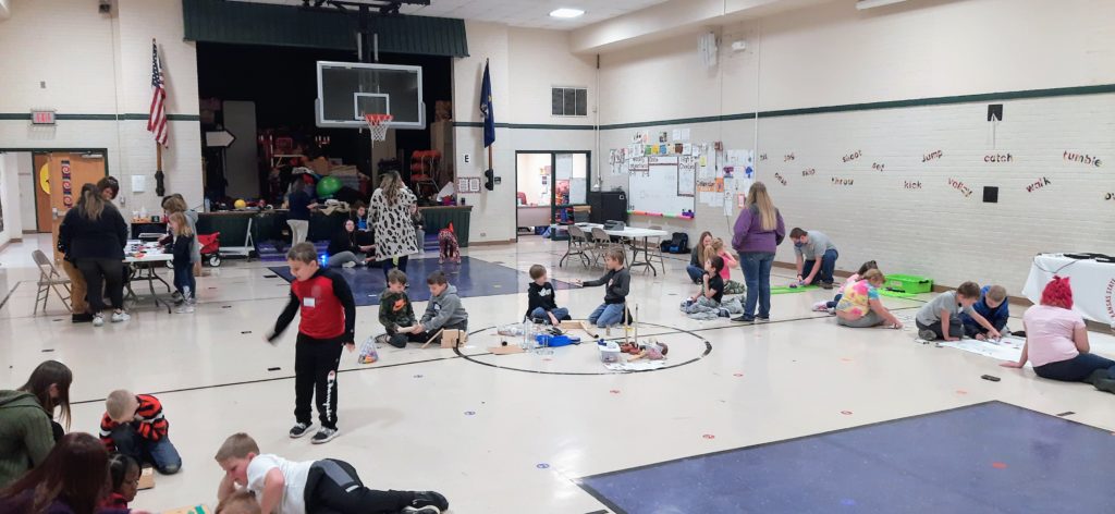 gym filled with students and teachers are different STEM stations throughout the gym
