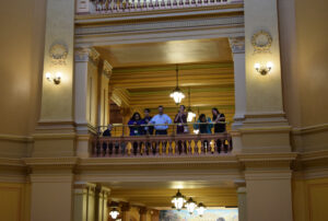 Students and teachers stand at a second floor balcony in the capital building.
