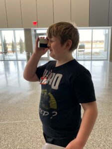 A boy holds a handheld telescope to his right eye.