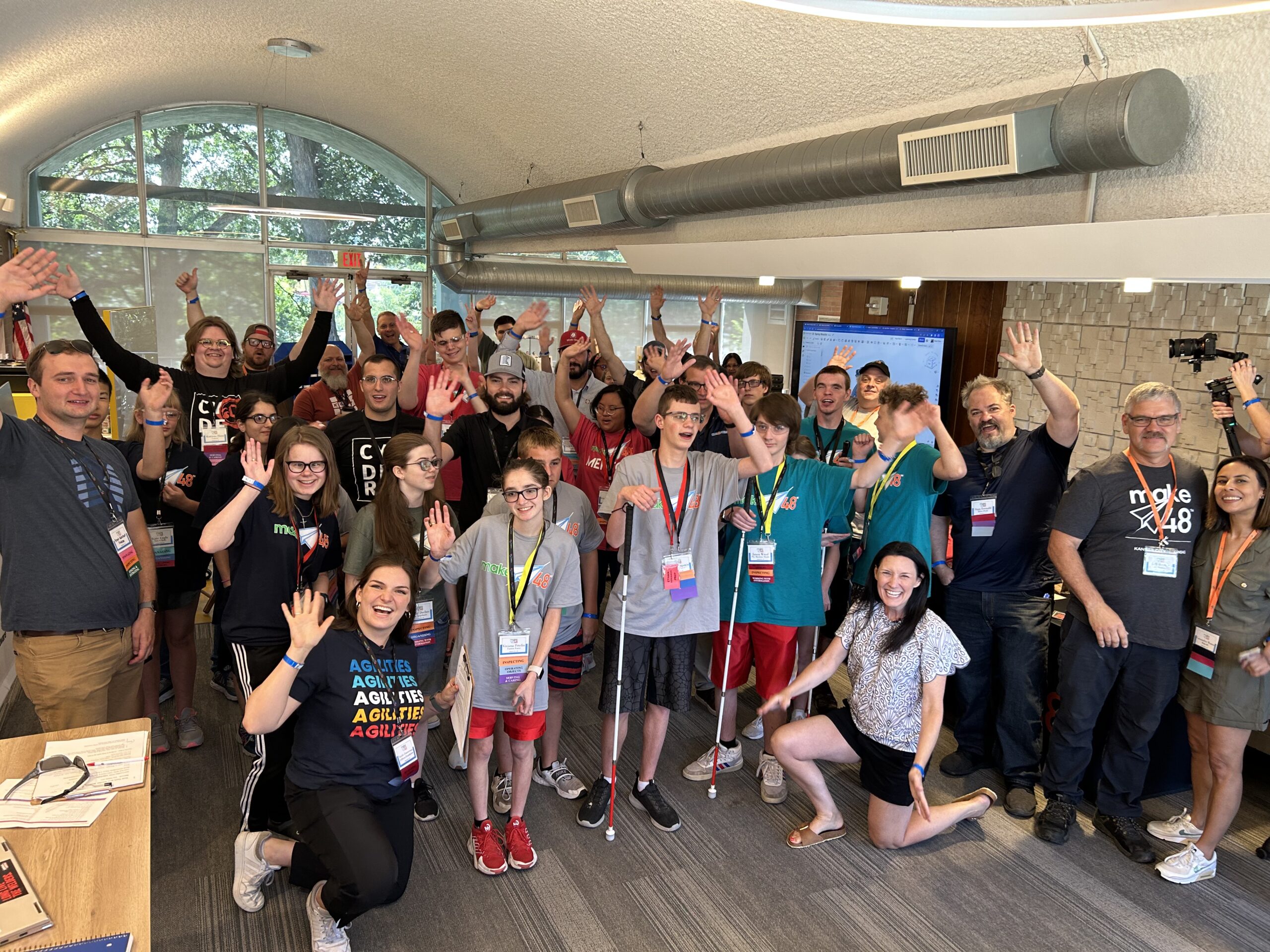 A large group of students and adults stand in the Makerspace, smiling wide and celebrating