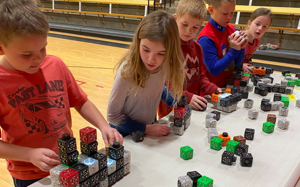 Students are lined up at a table in the gym as they build various robotic structures that light up