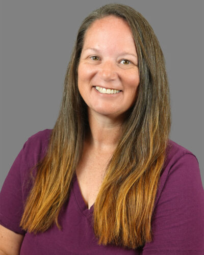 Mandy Smith has long brown hair, wears a purple shirt and smiles at the camera.